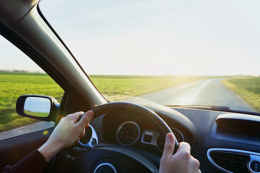 Driver's view of hands on the steering wheel while driving on a rural road.